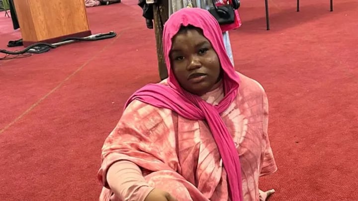 A woman in a pink head scarf sitting on the ground