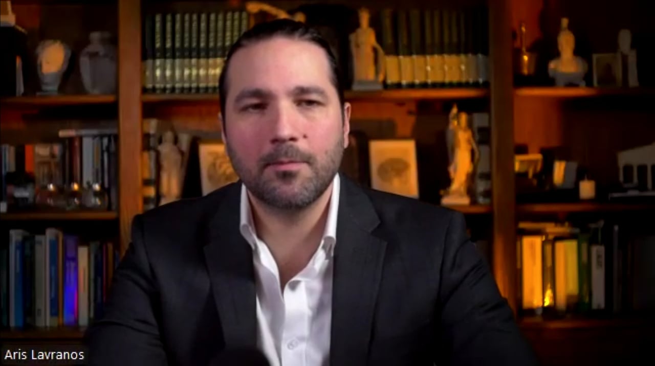 man in suit sitting in front of book case.