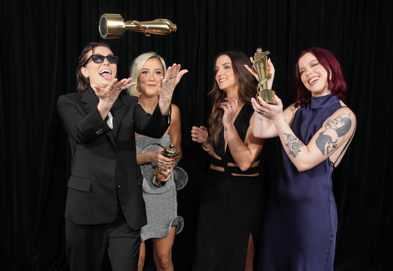 Four women from a musical band pose with statuette awards.
