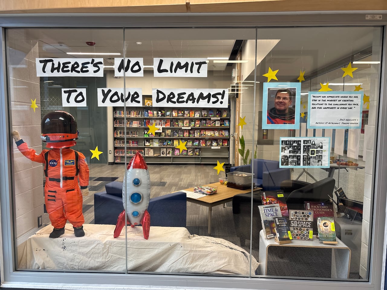 A display inside a school library window featuring a small astronaut figure, a rocket model, and space-themed books with a sign reading “There’s no limit to your dreams!” honouring astronaut Jeremy Hansen.