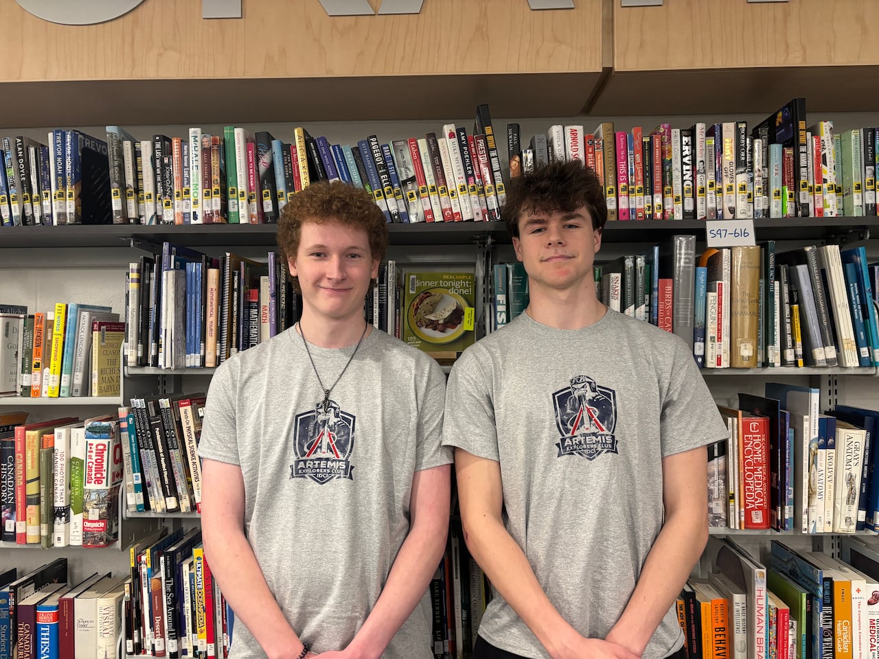 Ryan Knox and Gavin Laidman stand in front of bookshelves in a school library wearing Artemis II Explorers Club T-shirts.