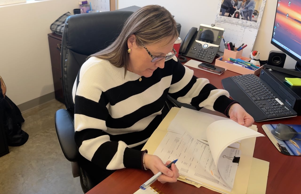 A woman sits at a desk while going through papers.