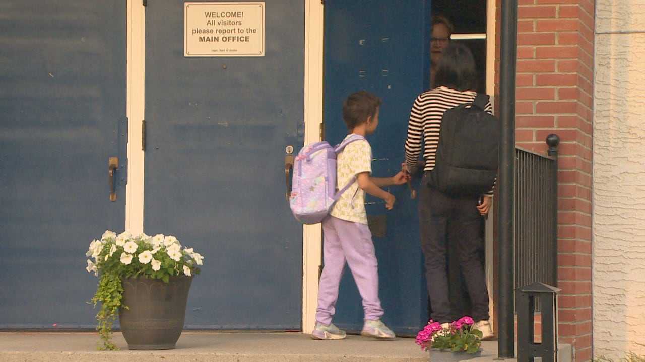 A child and an adult stand at a half-open door to a school