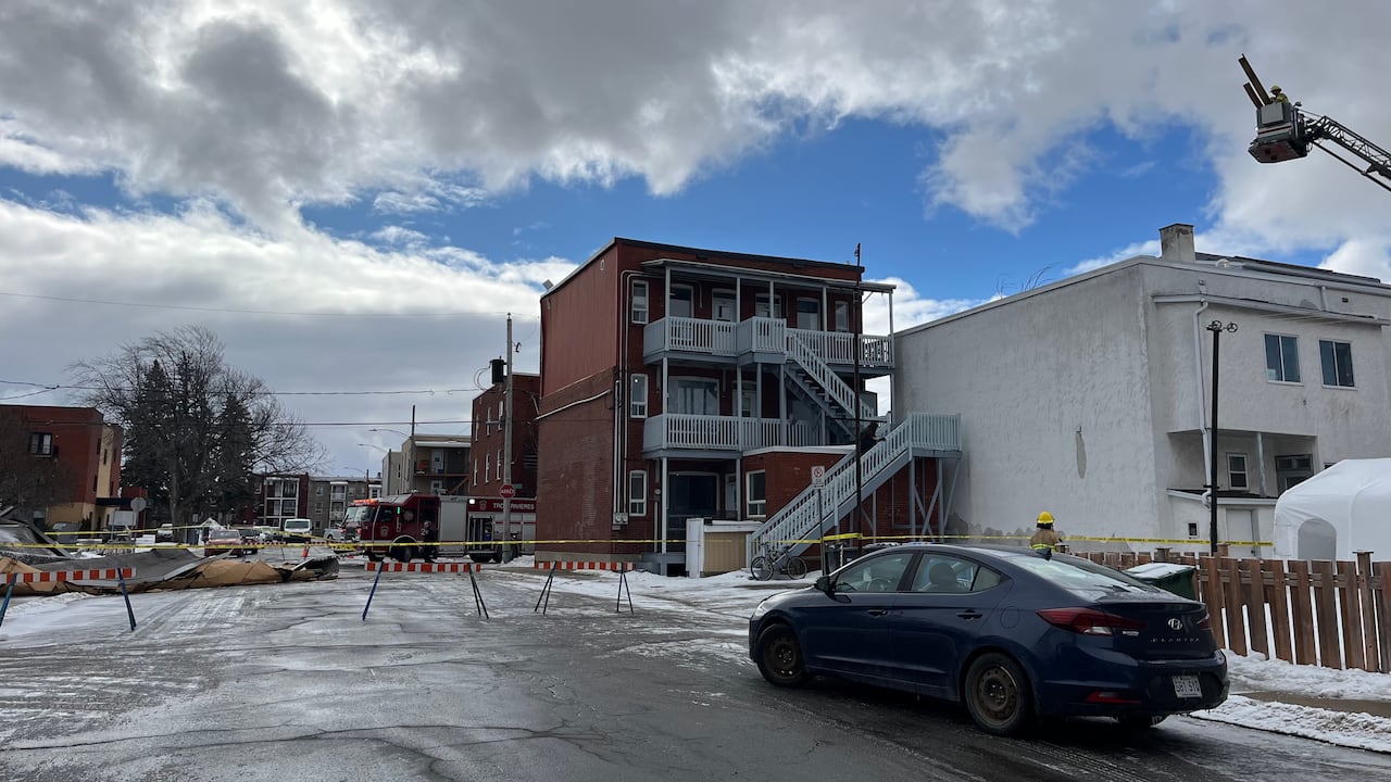 A street with residential buildings is closed off with barriers protects the area where a roof blown off by high winds landed on the road.