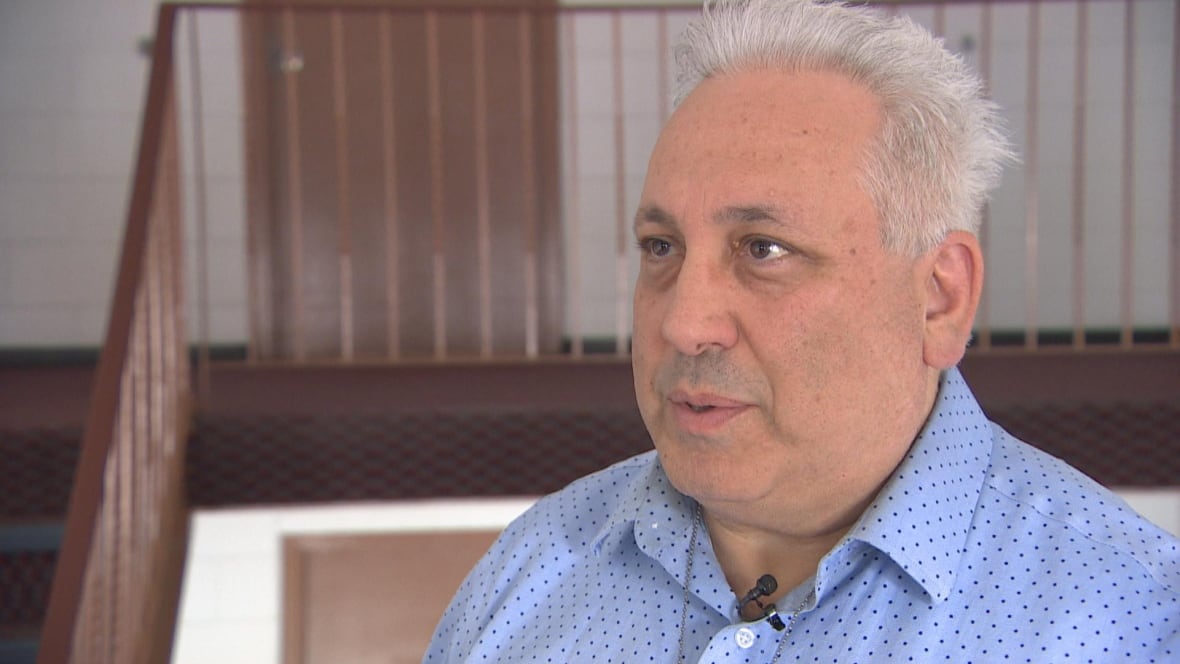 A man in a blue buttoned-up shirt stands on the second-floor foyer of an apartment complex.