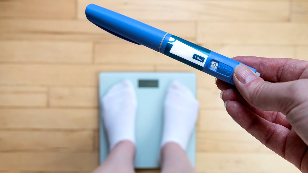 person stands on scale holding GLP1 injection