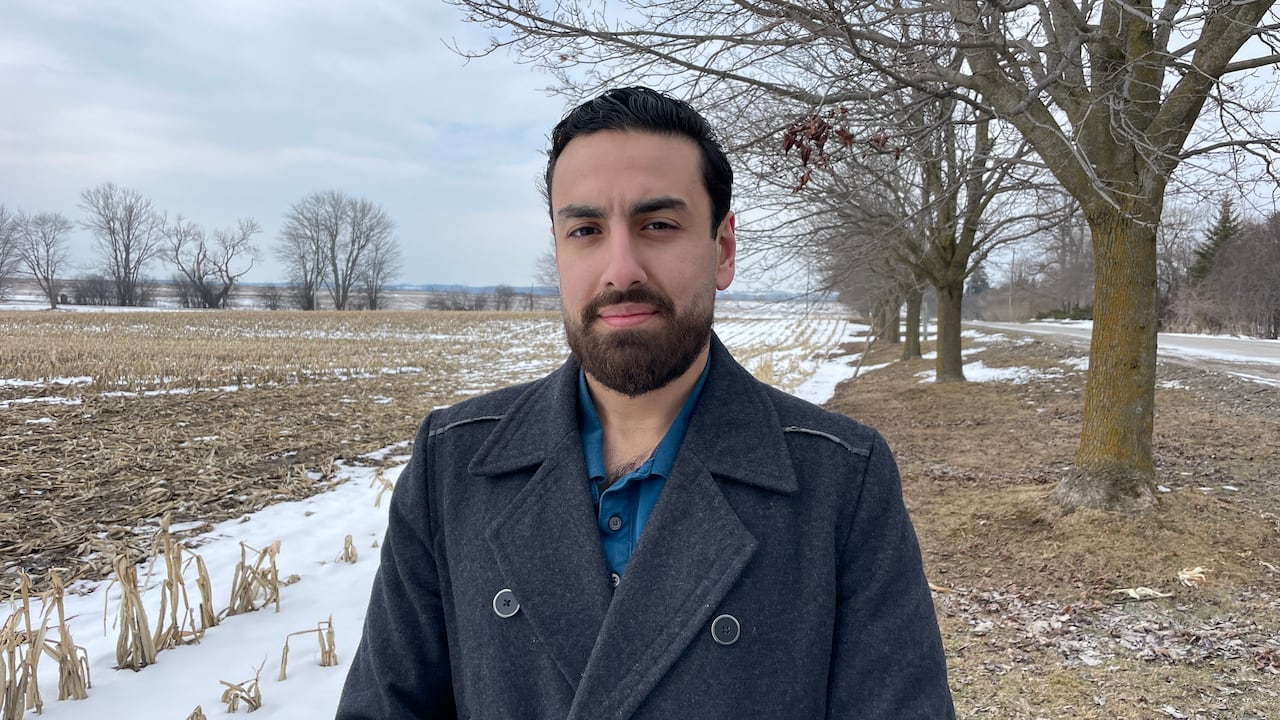 Photo of a man in a black jacket standing in front of corp crops in the snow