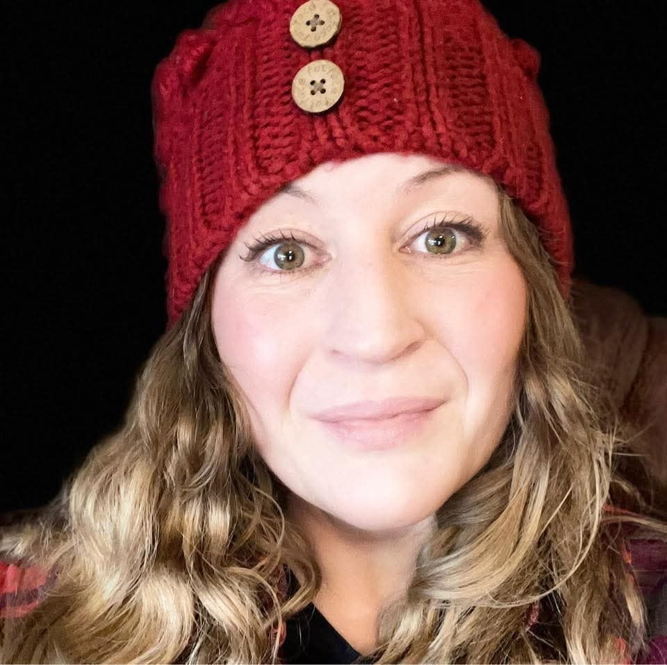 A blond woman wearing a knitted cap smiles.