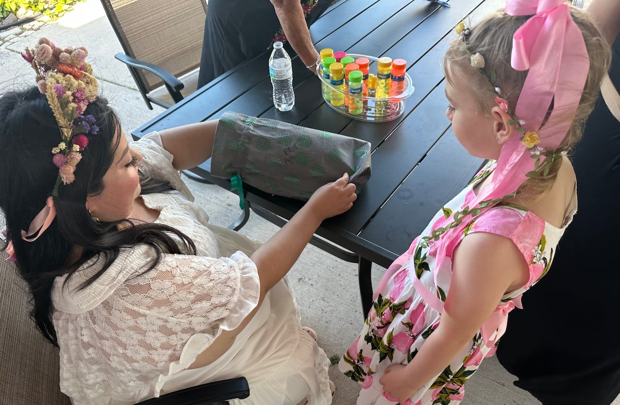 A little girl gives a present to a woman in a white dress.