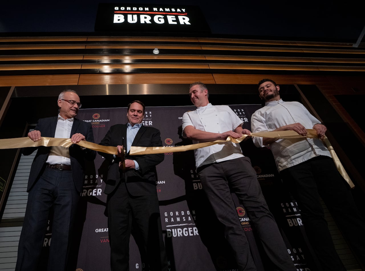 A group of people cut a ribbon next to a banner marked 'Gordon Ramsay Burger'.