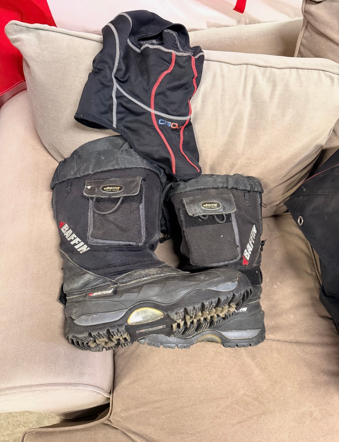 Black winter boots and a ski mask sit on a lounge chair. 