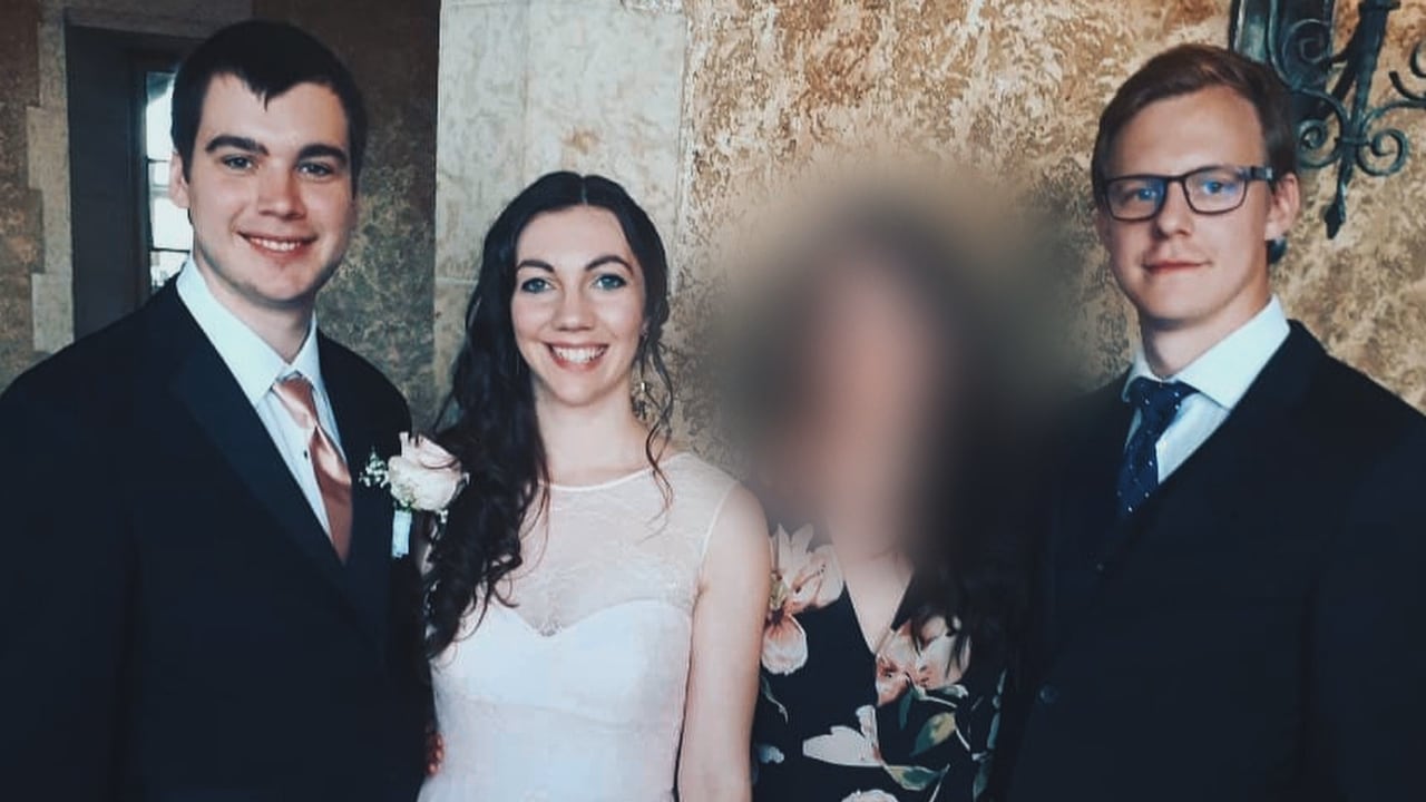 Two men in dark suits and a woman in a white dress smile for the camera.