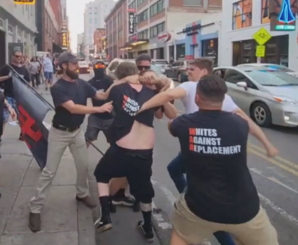 Men wearing black t-shirts fight on a busy street