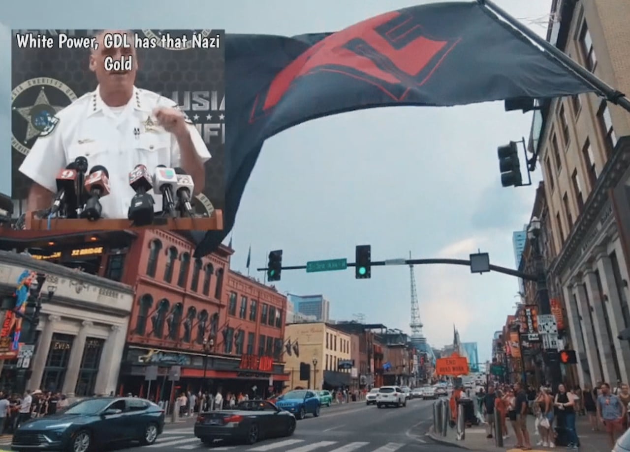 A screengrab of a livestream showing a busy intersection and part of a flag pole and a black flag with red insignia.
