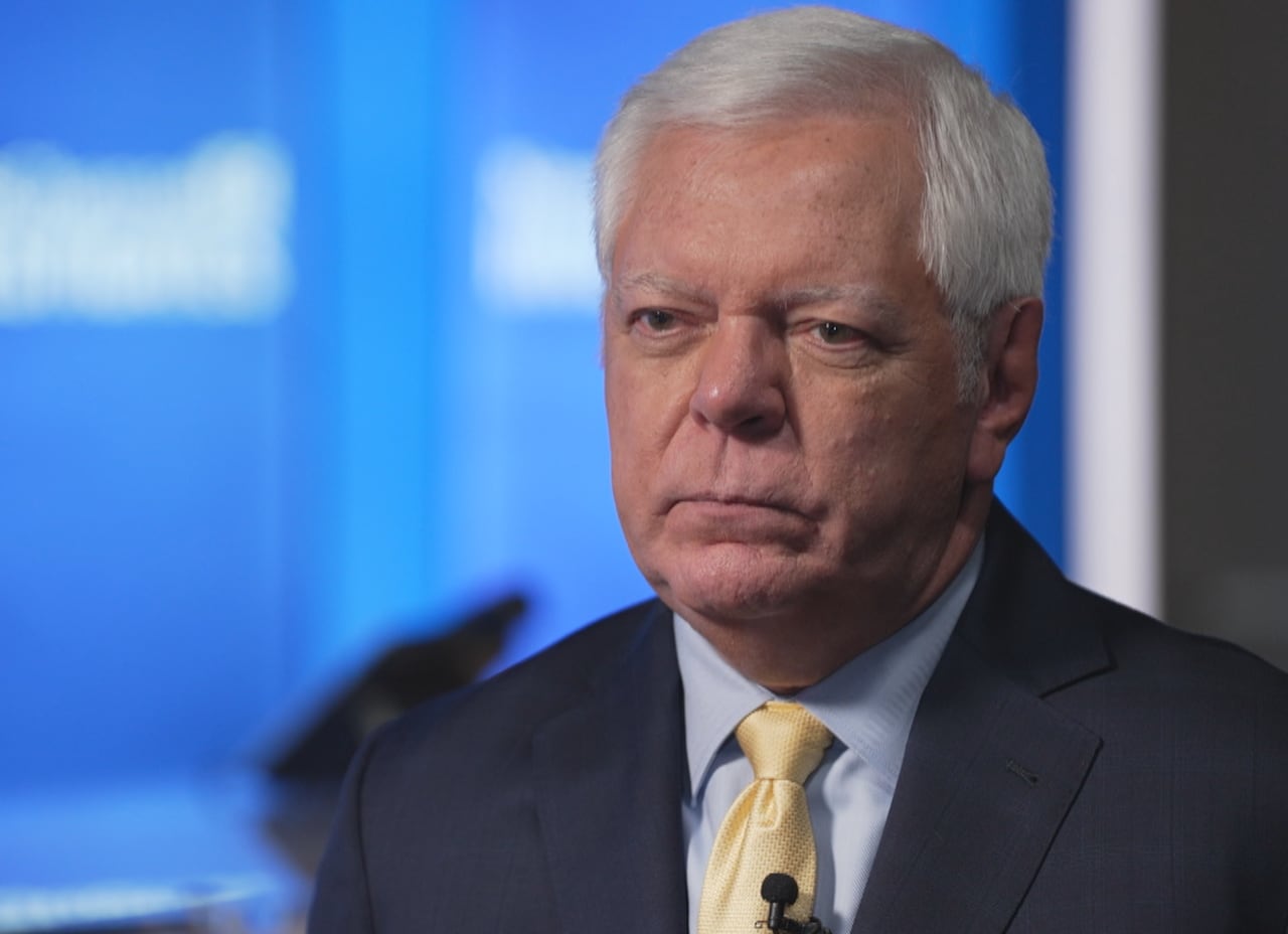 A group of men in red and black t-shirts set-up a large cloth banner by the side of a road.