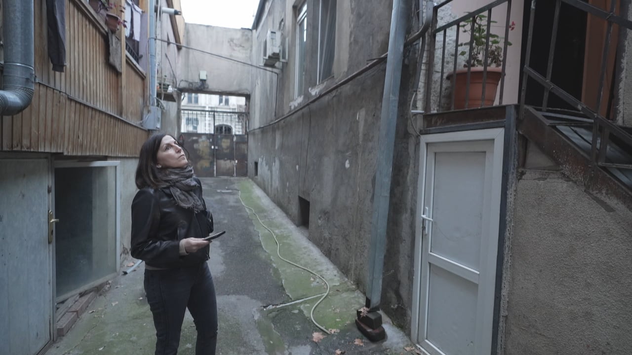 A woman stands in a wide laneway between two apartment buildings.