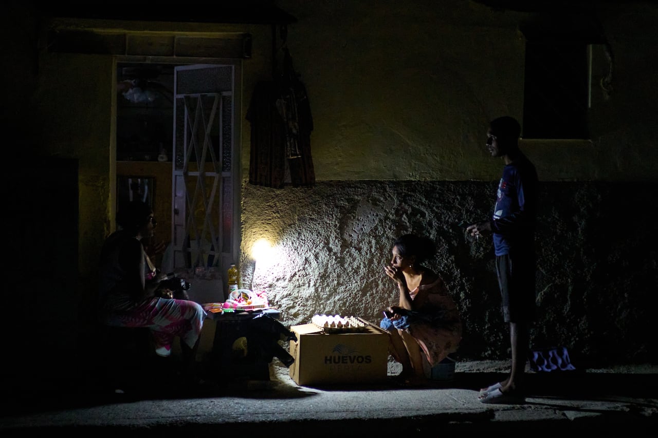 People sit outside at night on the street in the dark.