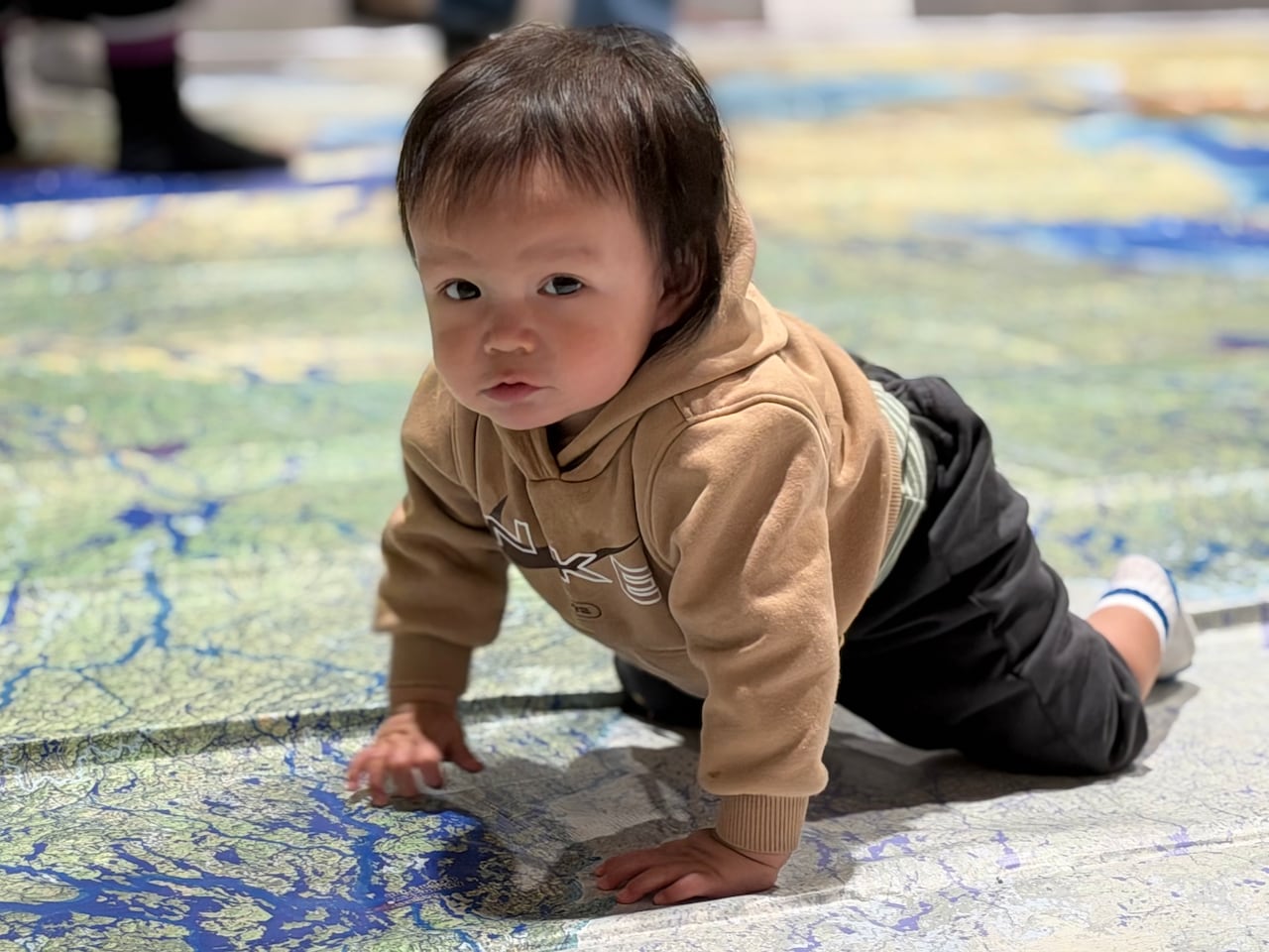 A baby crawls on a large map placed on the floor