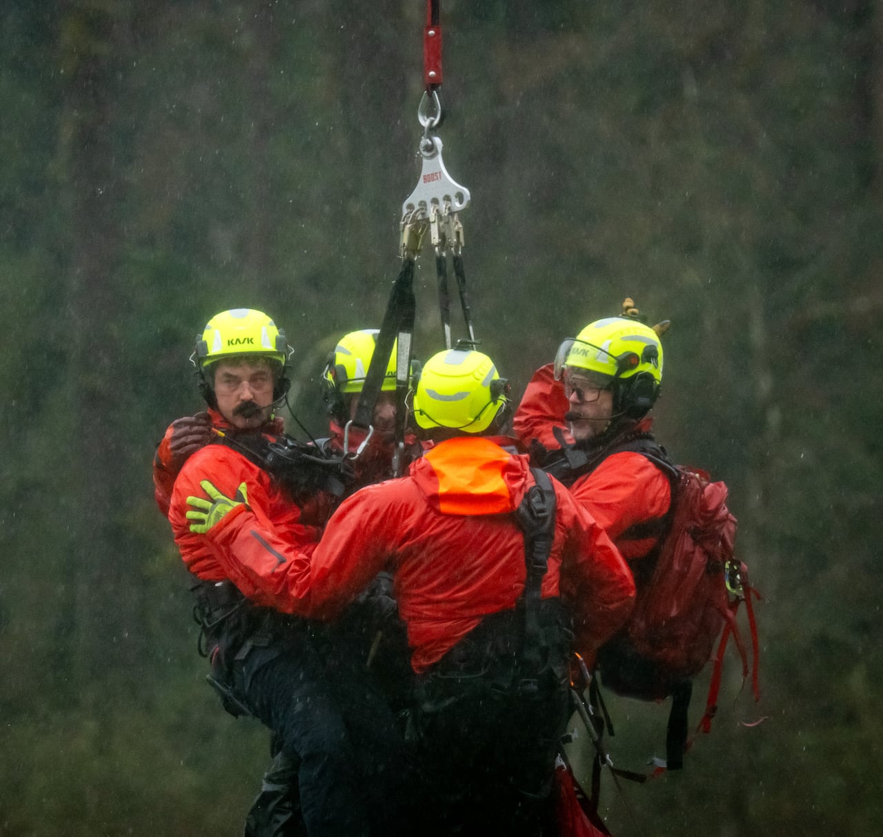 Men wearing hard hats are seen on a helicopter winch.