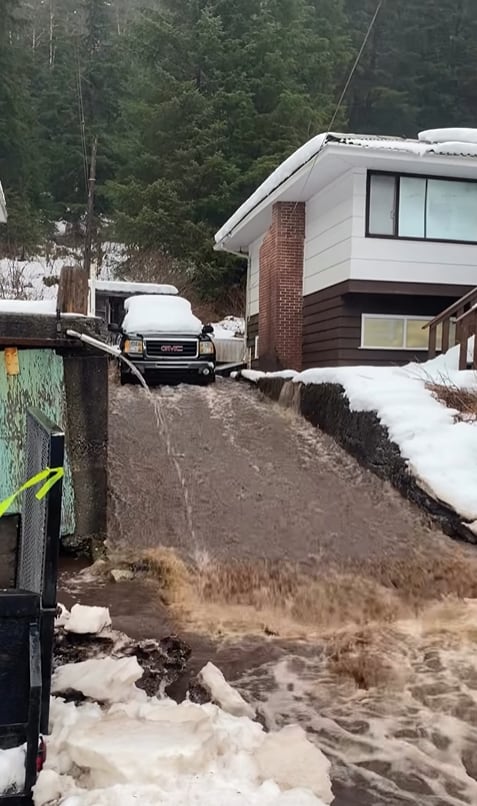 Water floods out of a home down a steep driveway of a home