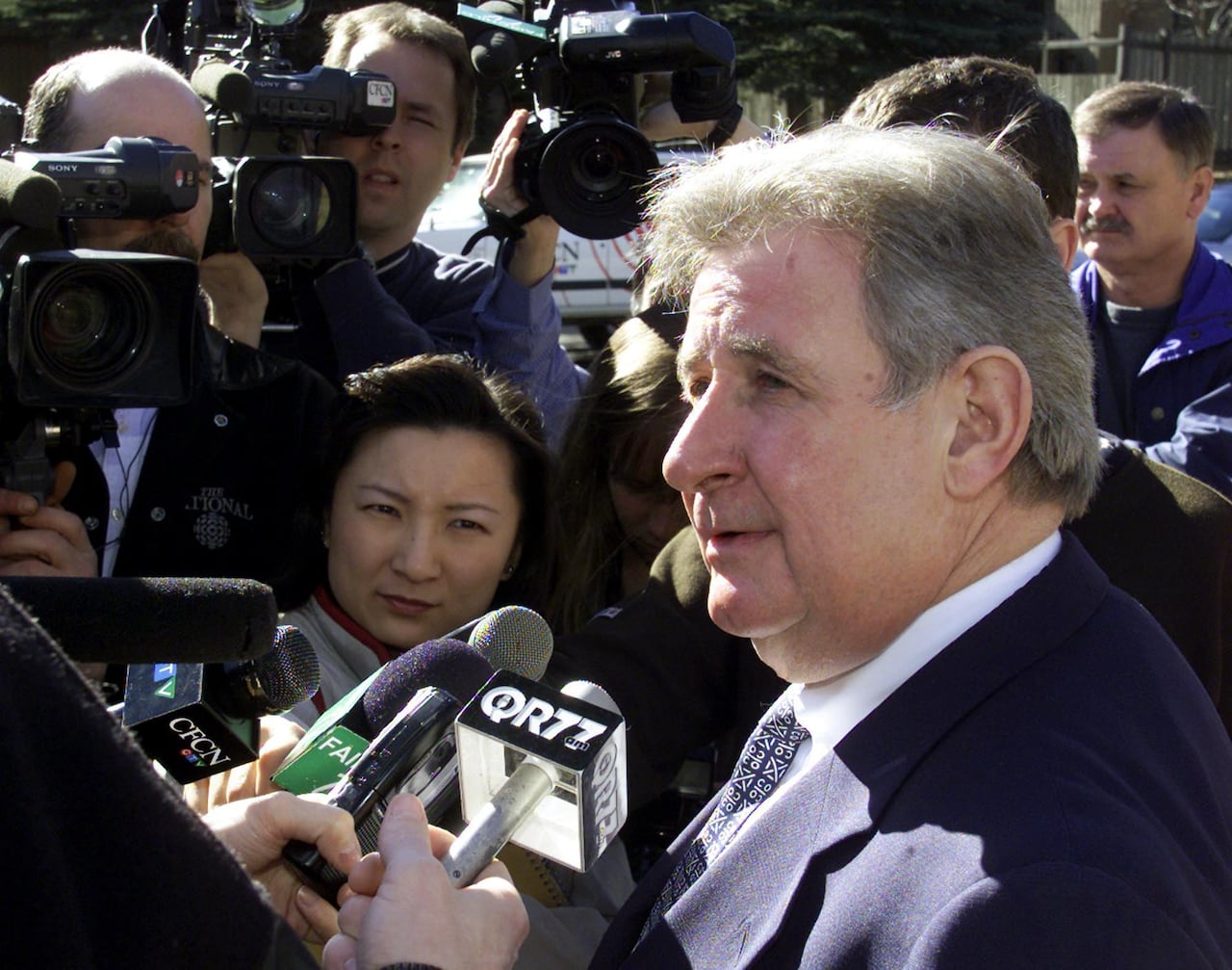 A man in a suit stands in a throng of reporters with microphones