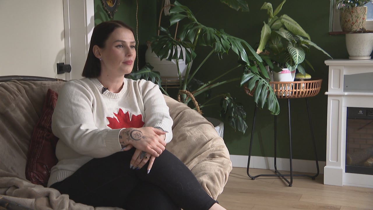 A woman wearing a maple leaf sweater sits in a chair.