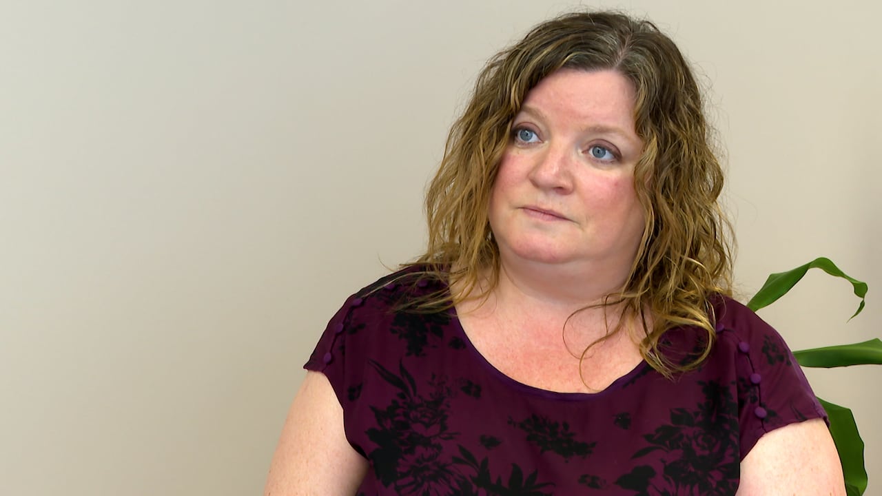 A woman in a tshirt and curly hair. She is in a conference room.