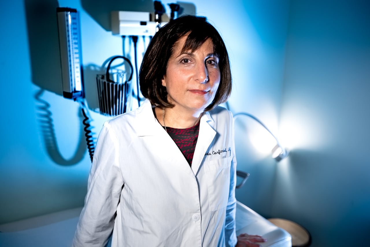 A woman in a lab coat poses for a photo in a doctor's office.