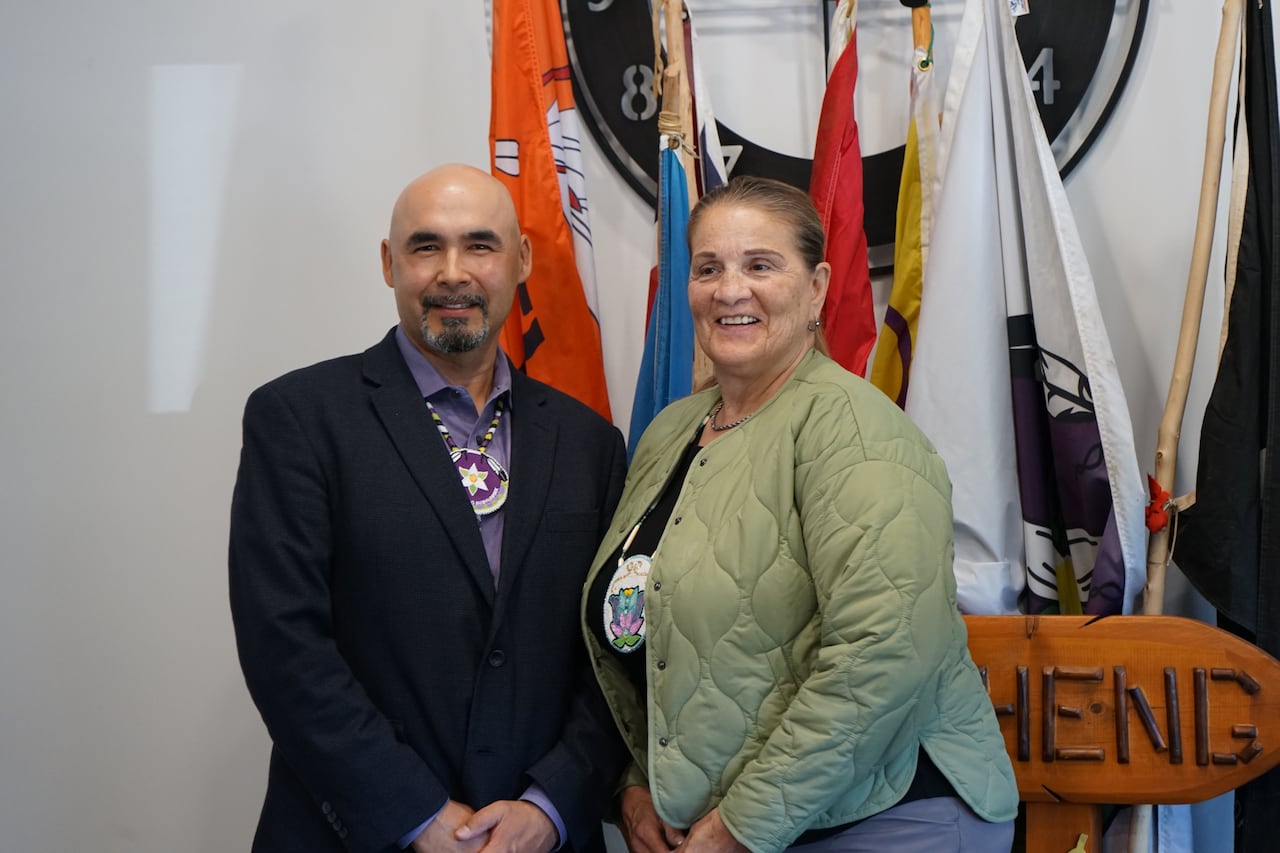 A man and woman standing in front of a podium with flags in the background.