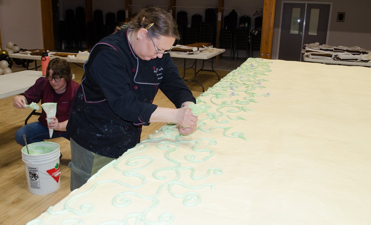 A woman applies icing to a massive cake.