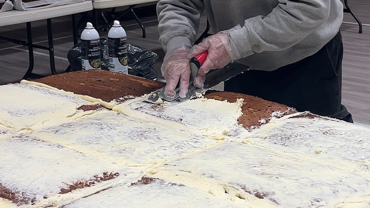 A person uses a scraper to apply icing to a massive series of cakes.