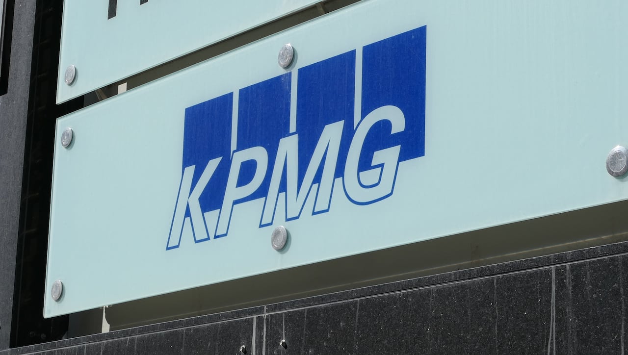 A closeup shows a sign on a building reading K-P-M-G.