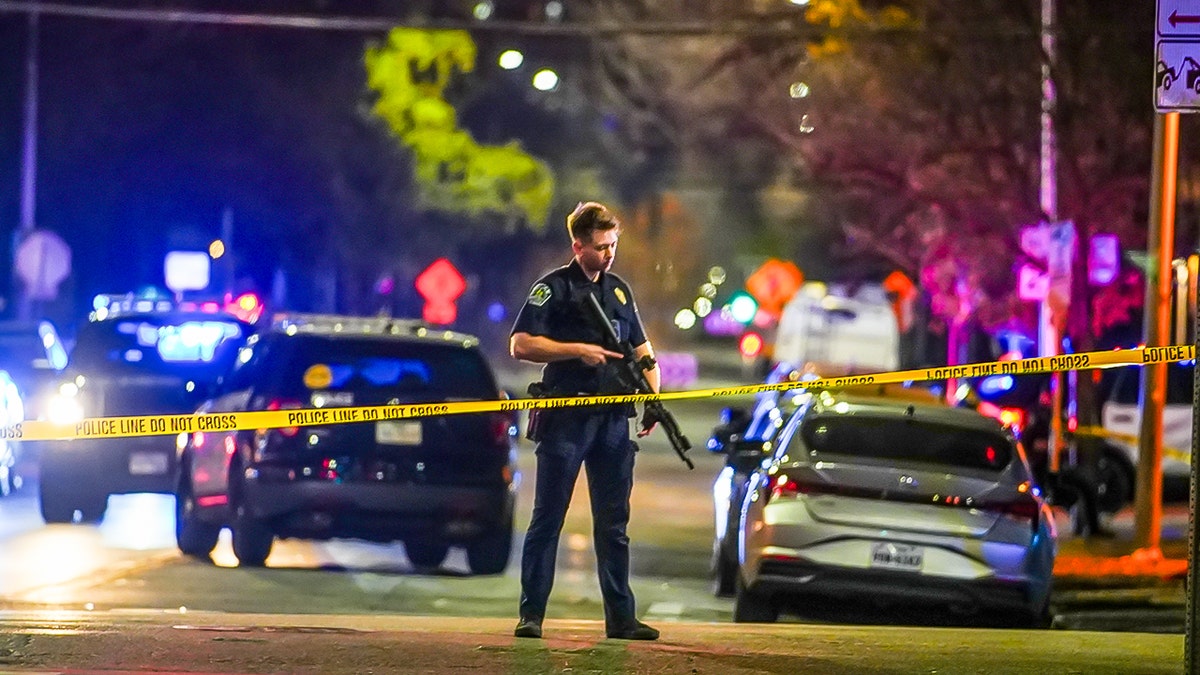 A lone officer on the street, behind caution tape, holding a rifle.
