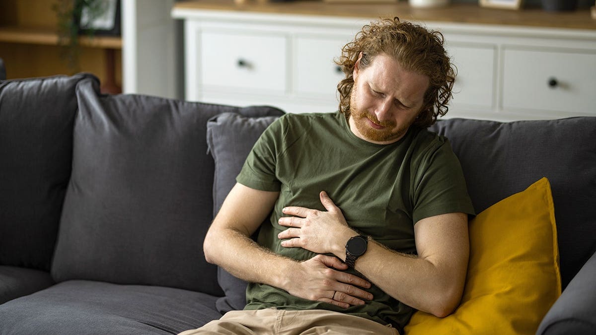 Depressed young man holding his stomach while sitting at home.
