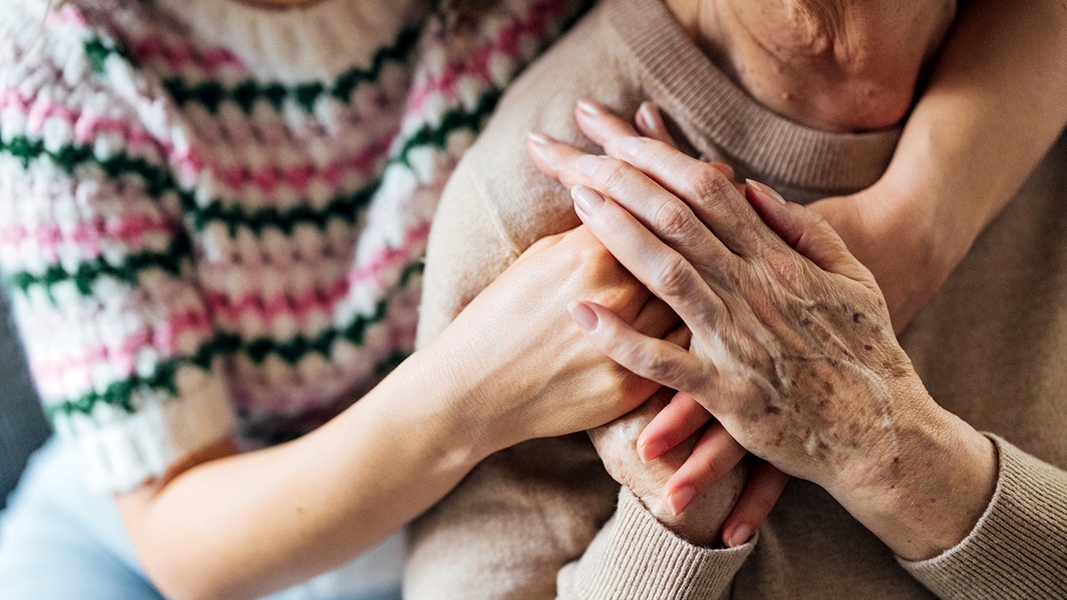 an elderly woman holds hands with a younger woman