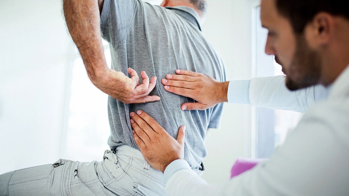 Senior man pointing to his lower back while sitting in a doctor's office with a male doctor.