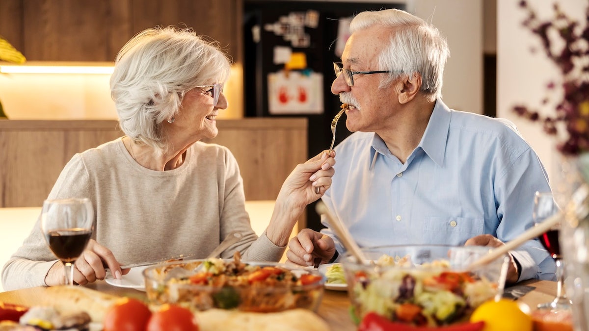 Senior woman feeding husband at table