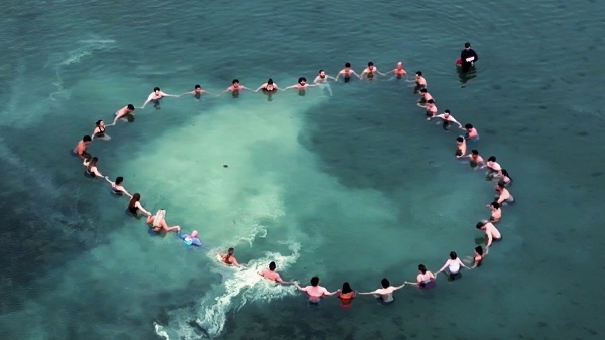 group holds hands in circle in the ocean