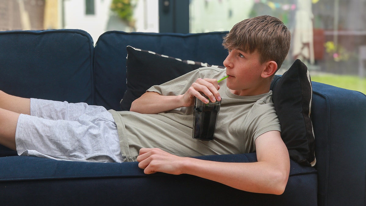 teen boy lays on sofa drinking soda