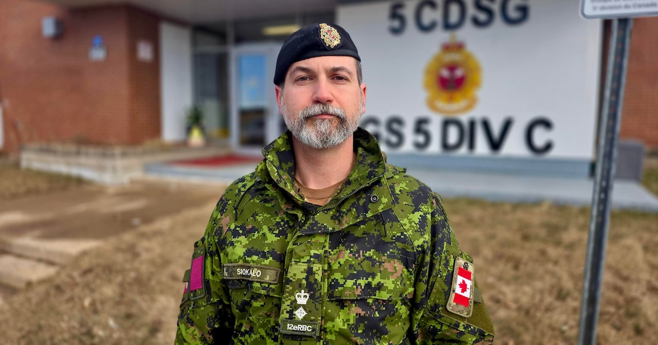 A soldier in uniform with a trimmed beard looks at the camera with a slight smile