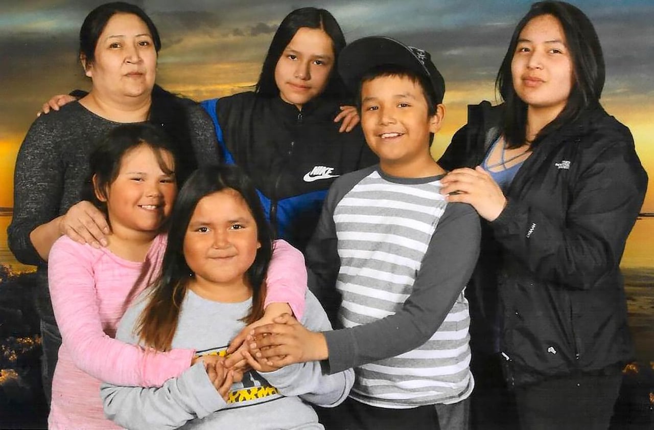 A woman, four girls and a boy smile for the camera in front of a sunset. 