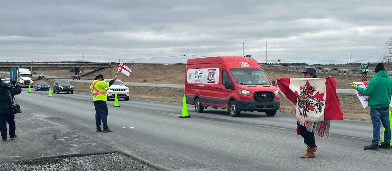 One lane of a two-lane highway is blocked by people holding Mi'kmaq flags