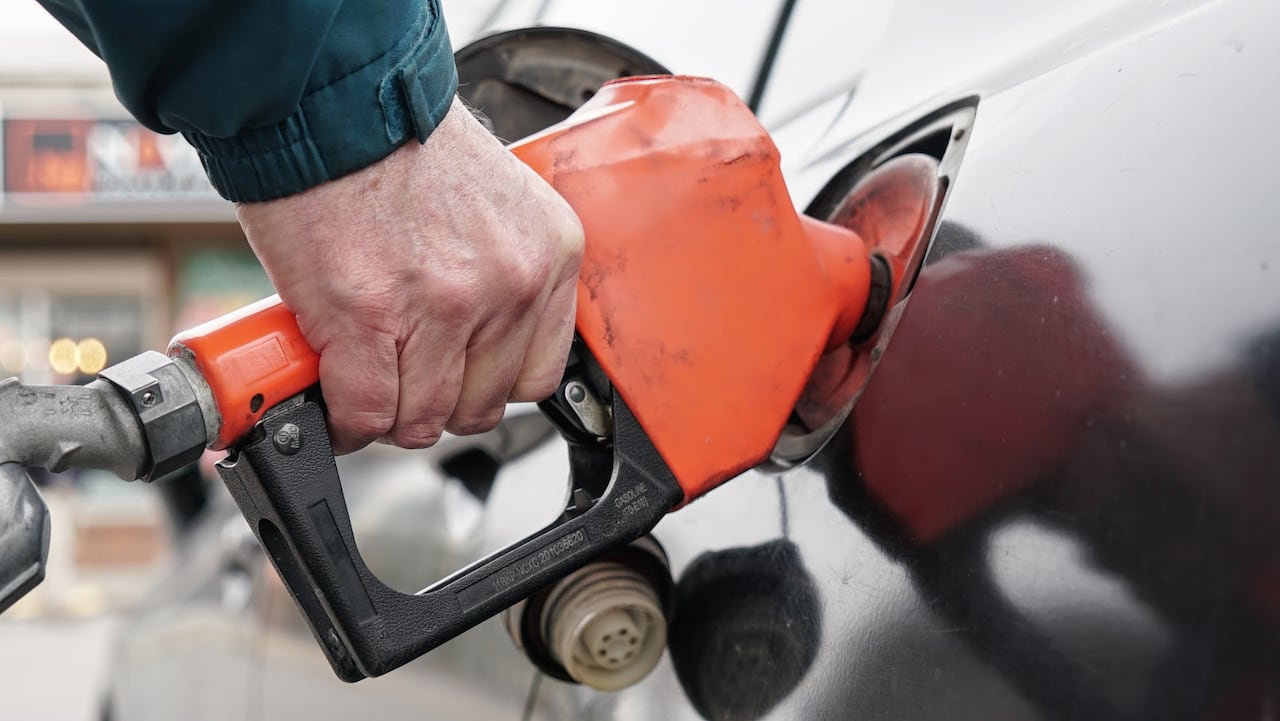 A hand is holding a red fuel nozzle that is inserted into a passenger car. 