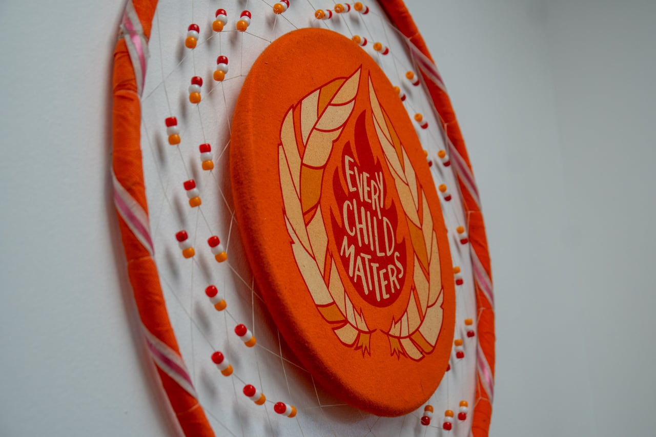 An orange dreamcatcher is seen on a wall. It says "Every Child Matters."