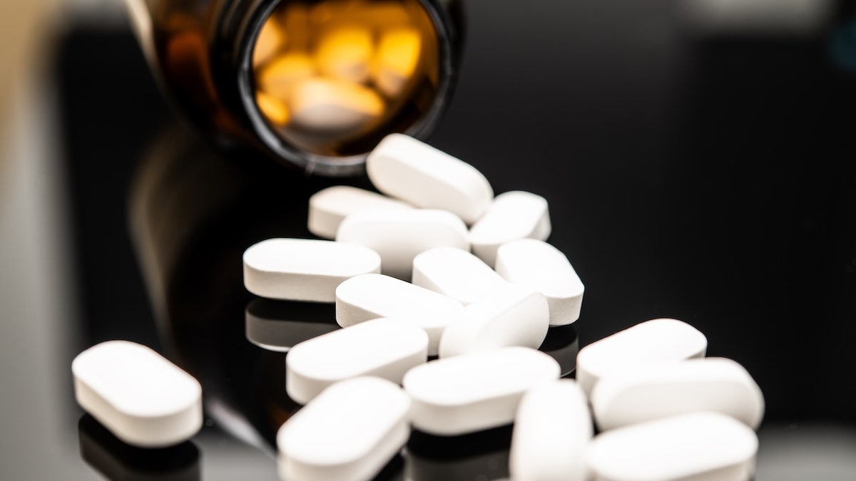 White opioid pills spilled from a dark amber prescription bottle on a reflective surface