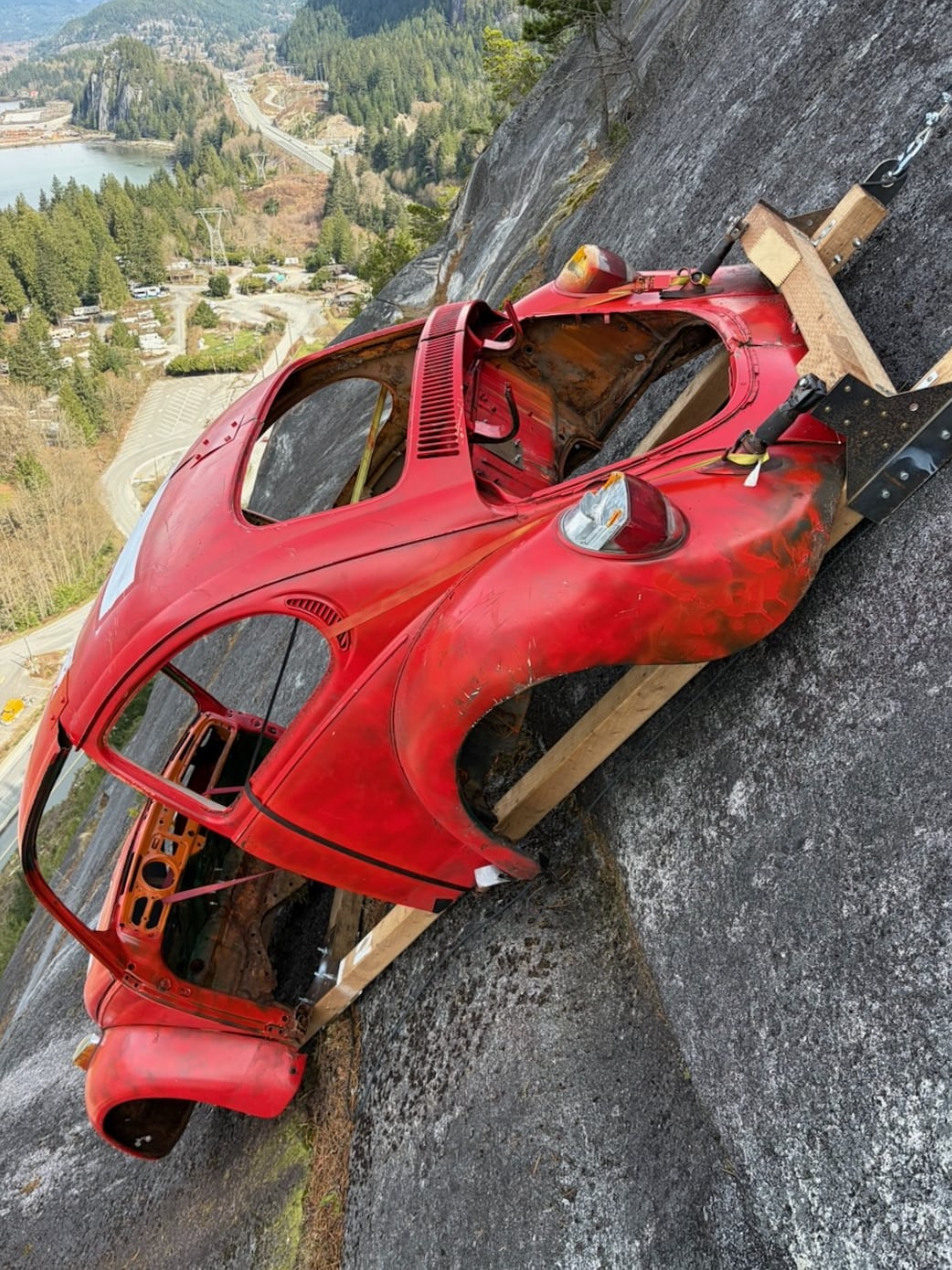 A red hollowed out car is pictured on a rock face.