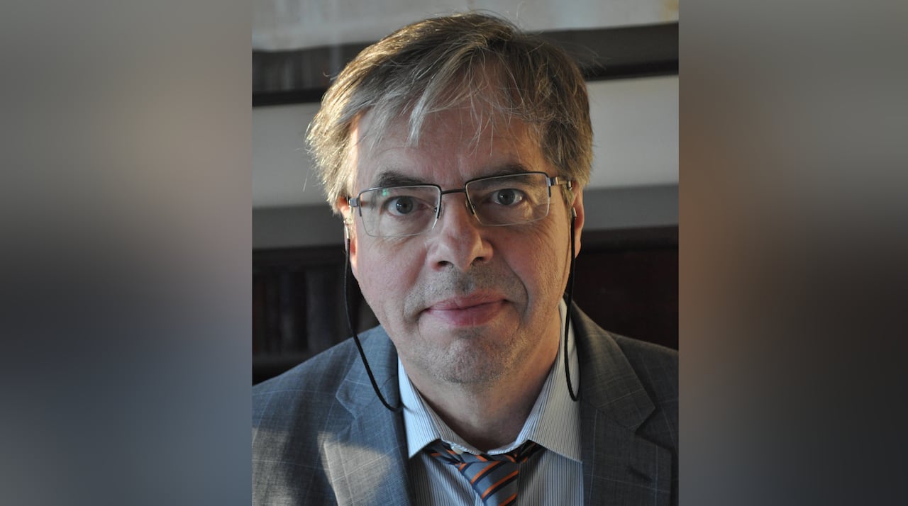 A man in a grey suit and tie looks at the camera.