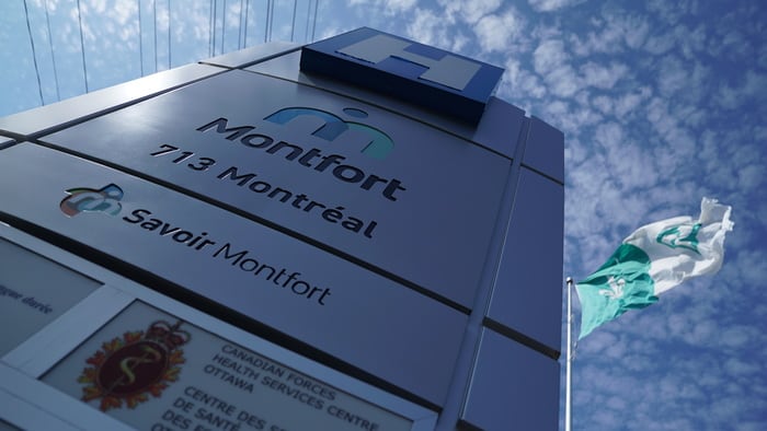 A sign for a hospital, with the Franco Ontarian flag flying behind it on a sunny day.