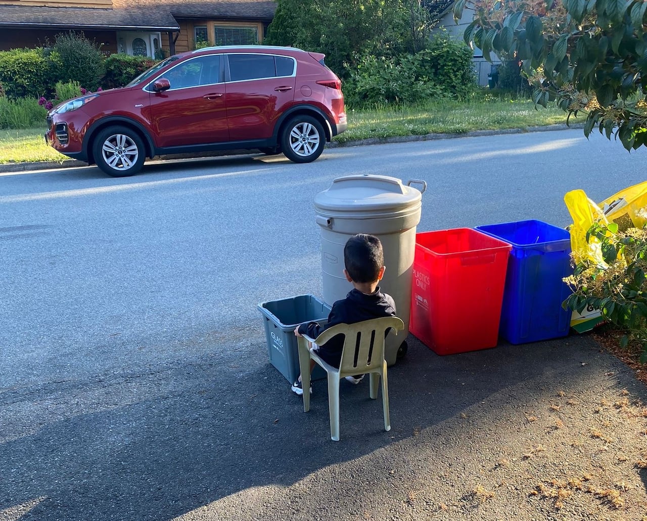 A child sits near the recycling on a suburban street.