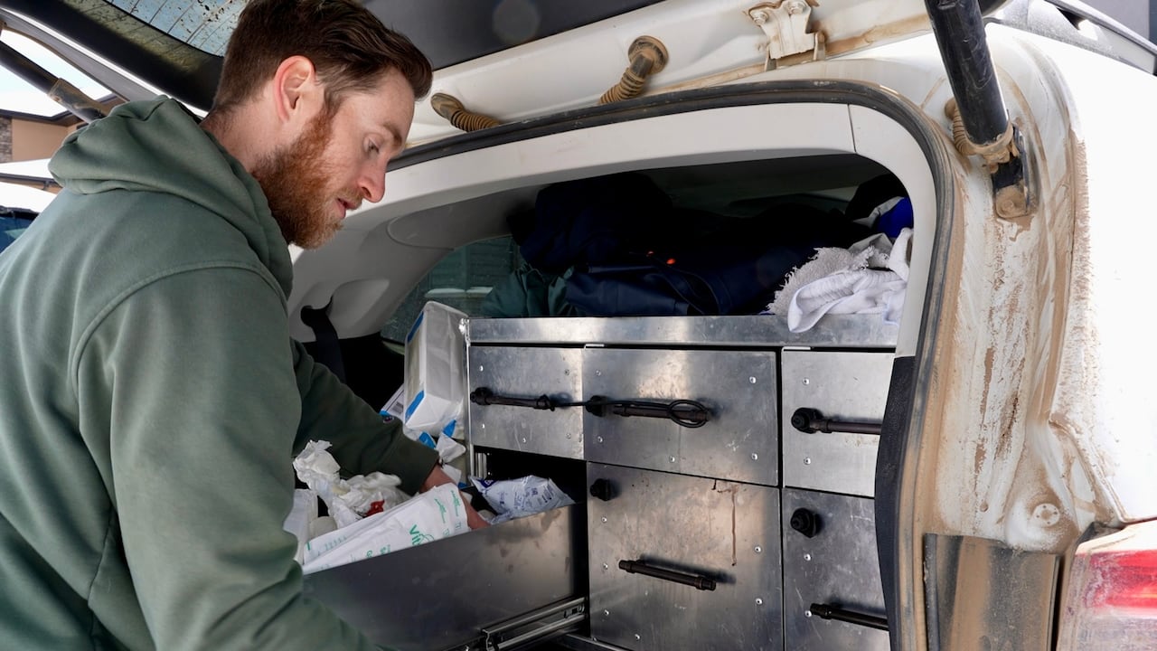 Man looking through a few drawers in his car trunk. 
